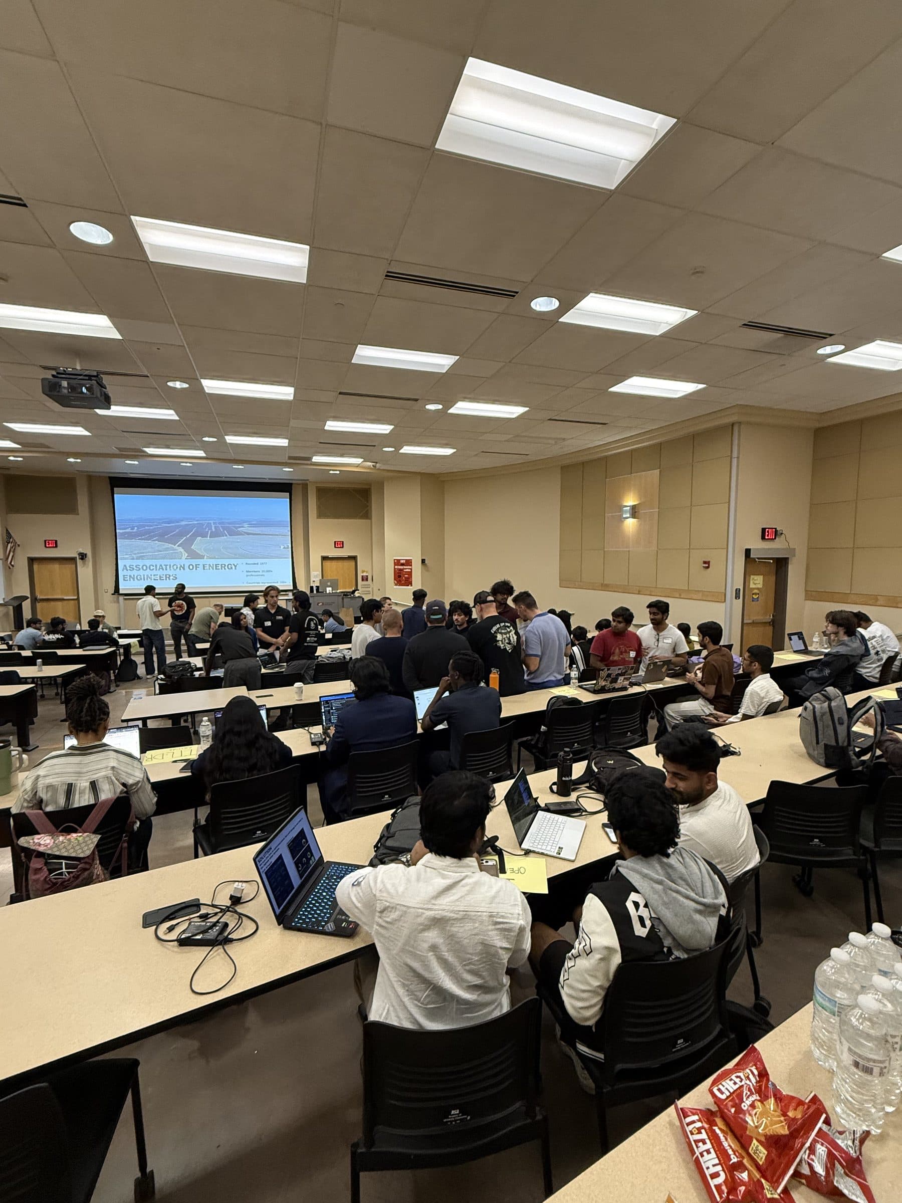 Teams working at laptops across the tiered benches of a full lecture hall during the hackathon.