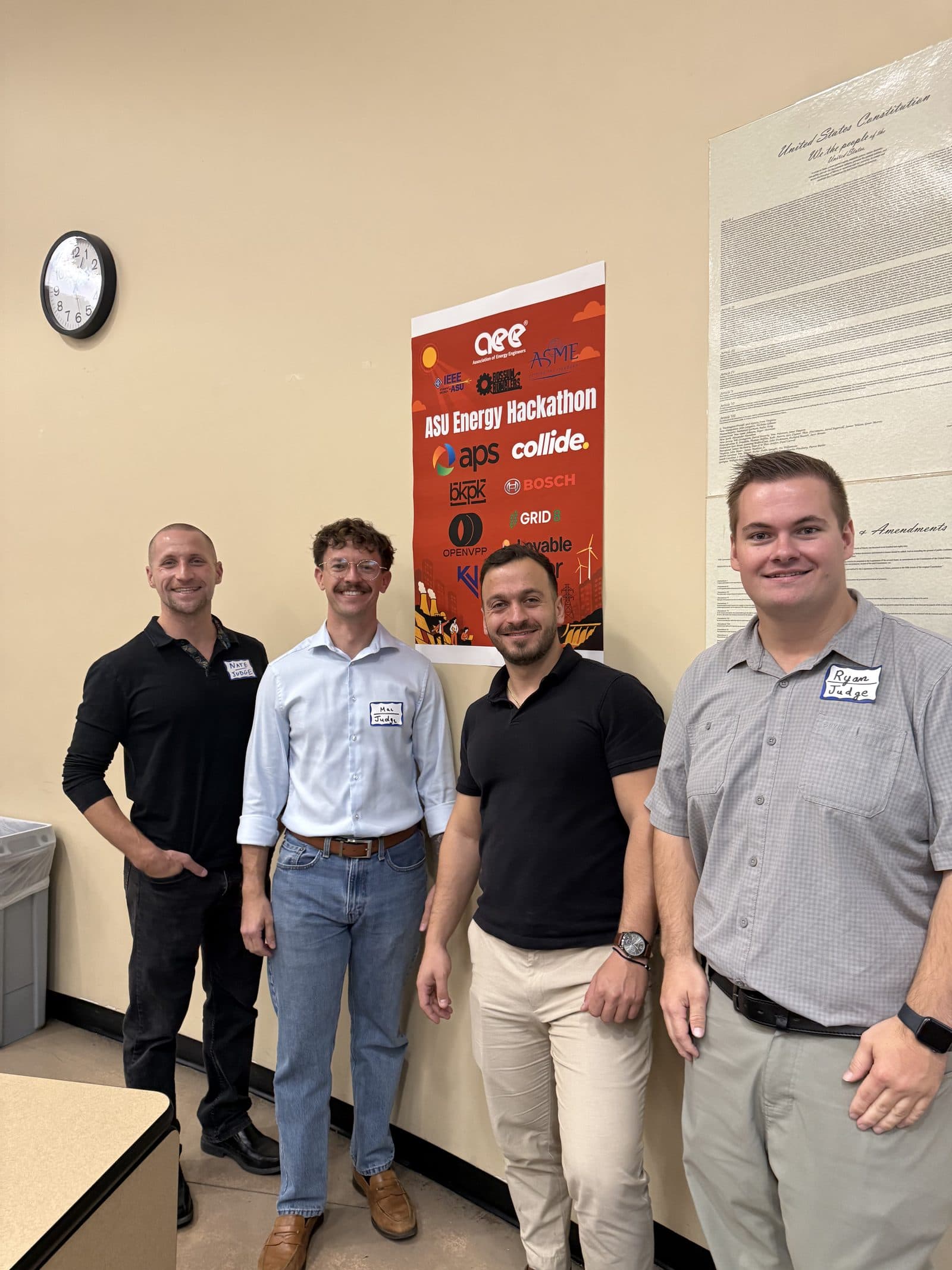 Four judges stand together beside the hackathon banner before judging begins.