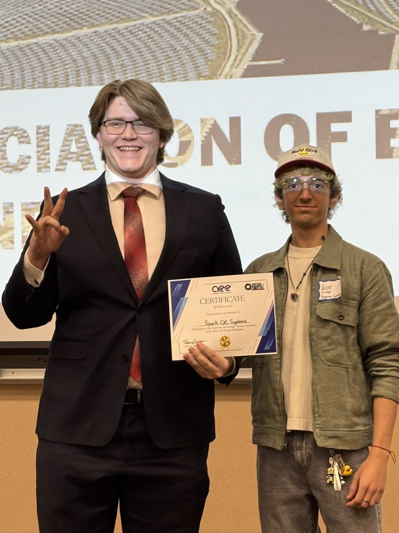 Two participants hold up their certificate and pitchfork hands in front of the projection screen.