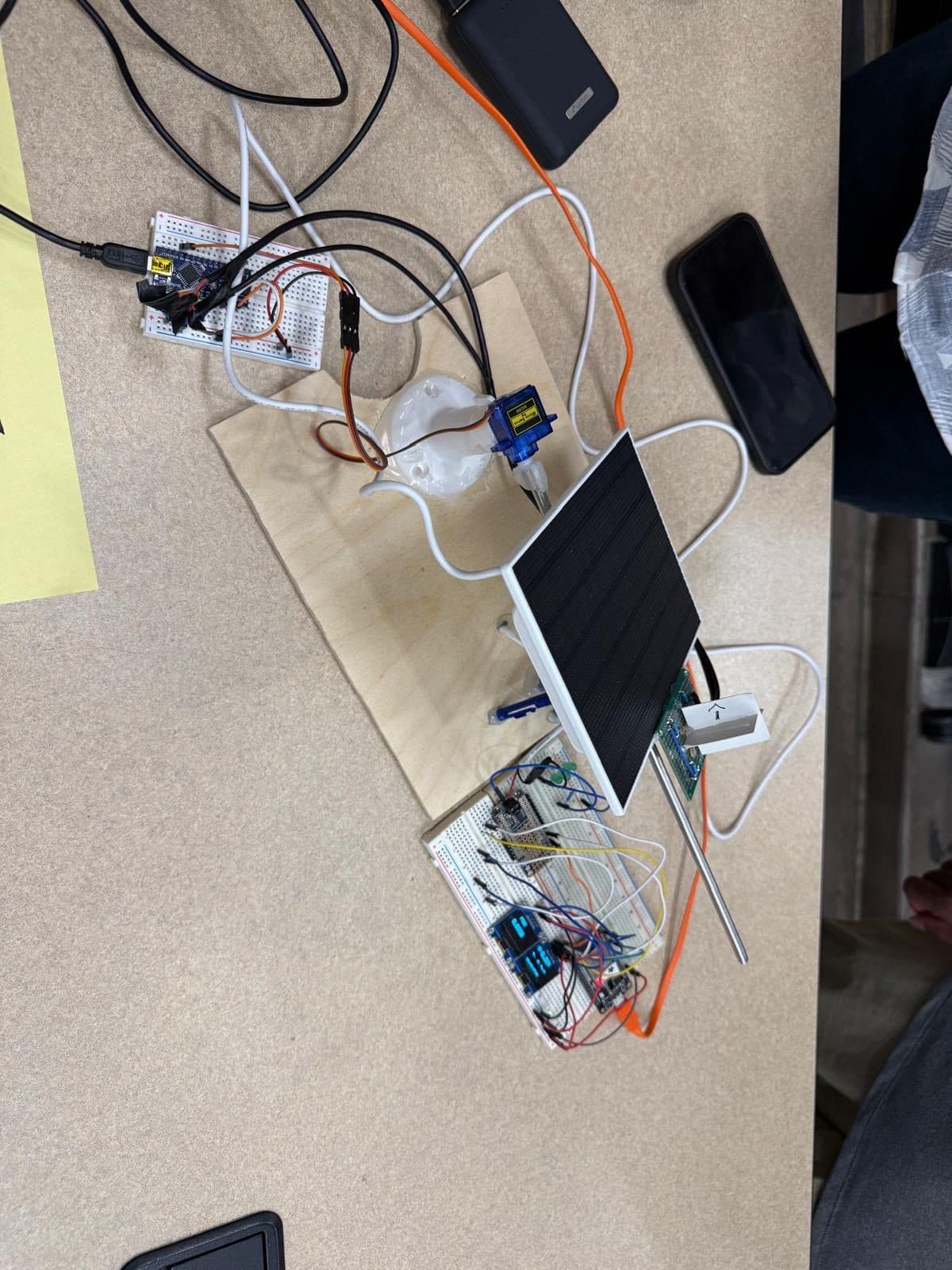 A hardware prototype on a table: a small solar panel wired to a breadboard and microcontroller.