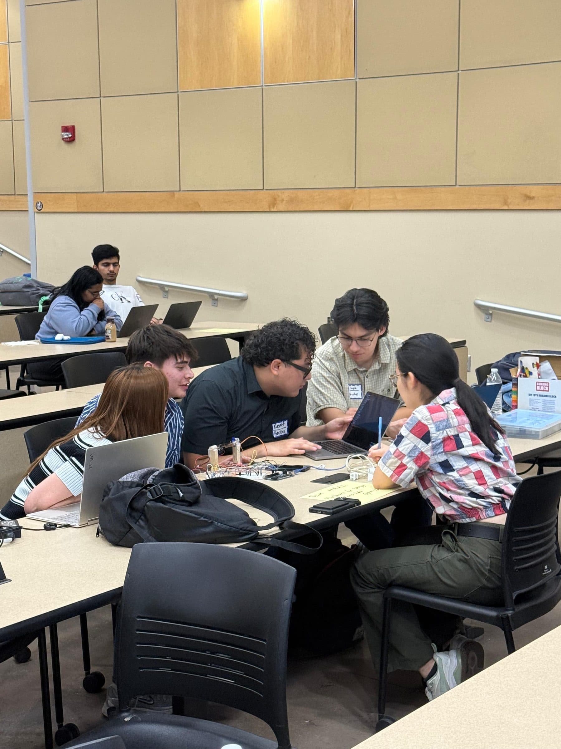Students seated around a shared table mid-discussion, papers and a laptop between them.