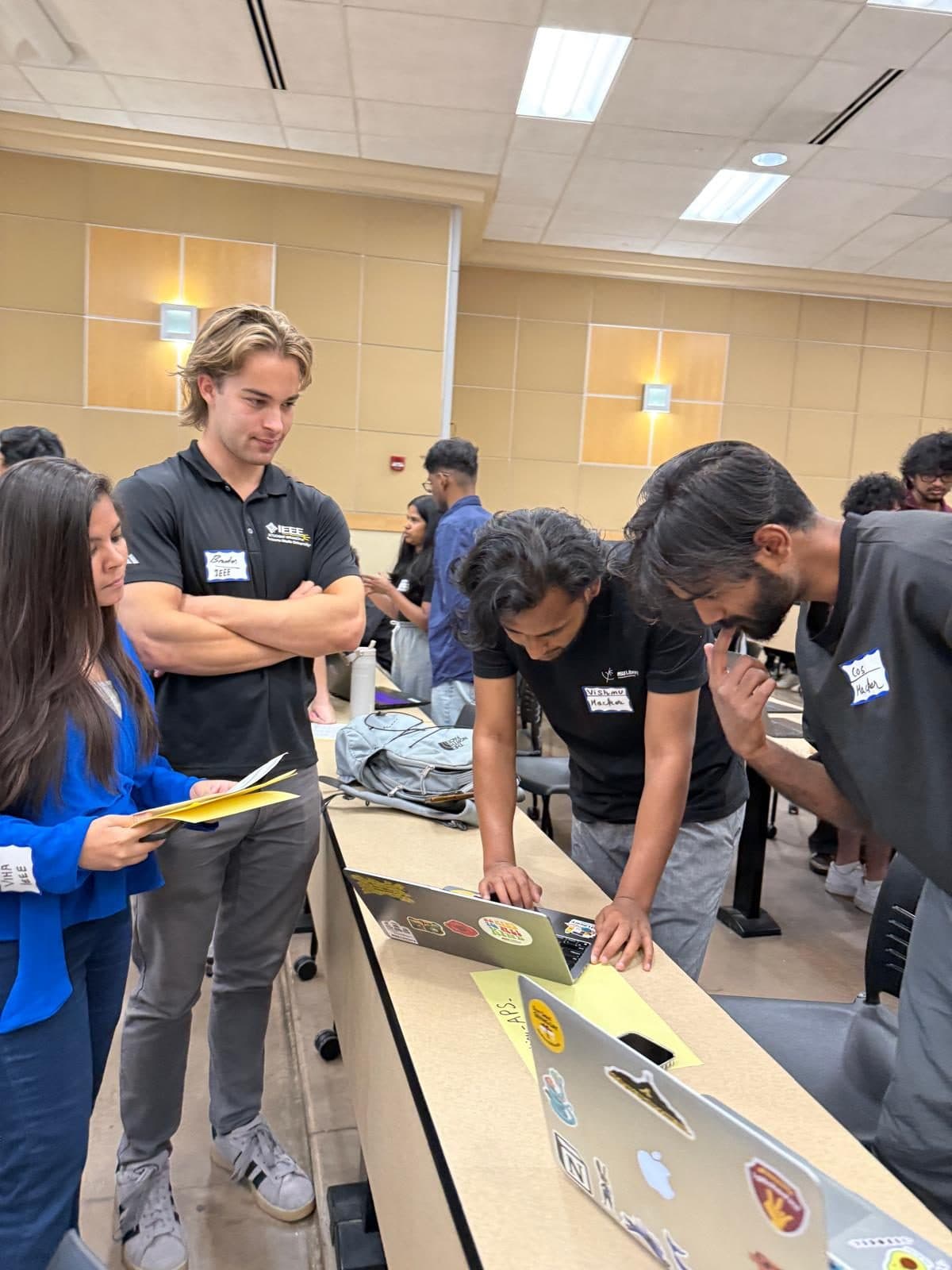 Participants and a mentor huddled around a laptop at a chapter event, with a volunteer taking notes beside them.