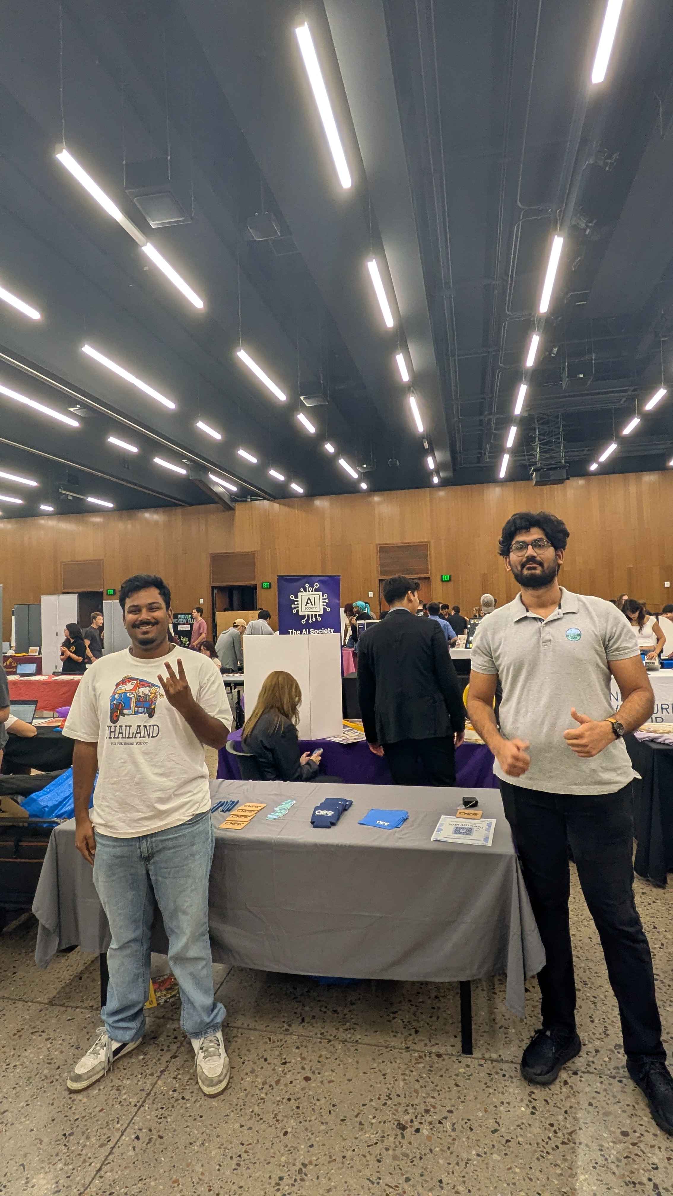 Two people stand beside the AEE table with chapter giveaways during an indoor student organization fair.
