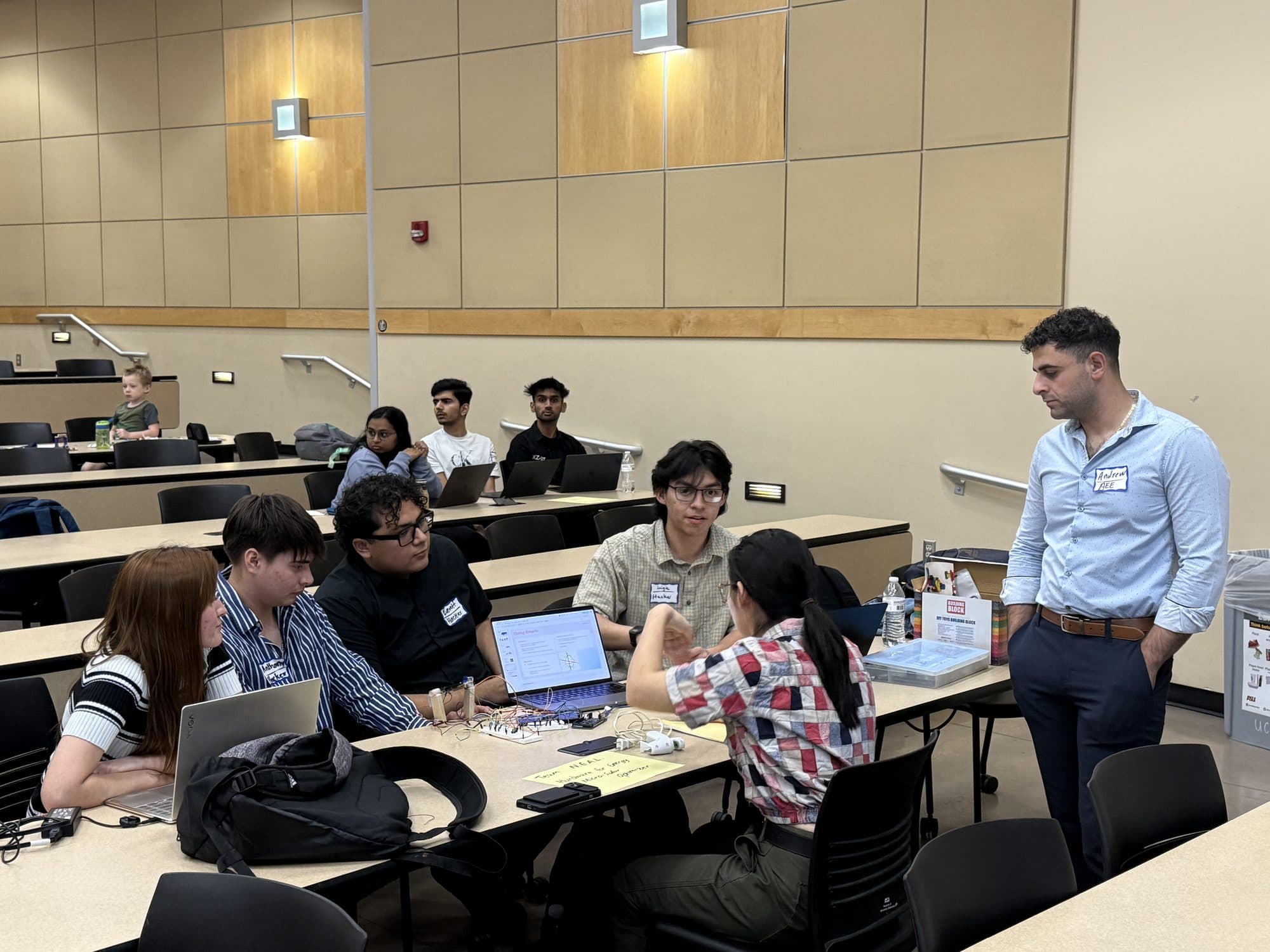 Students gathered around one end of a lecture-hall bench in discussion with laptops open in front of them.